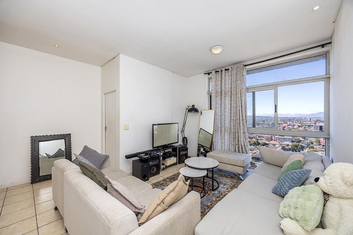 A bright living room featuring tiled flooring and a large sliding window offering expansive city views, providing a comfortable and well-lit living space.