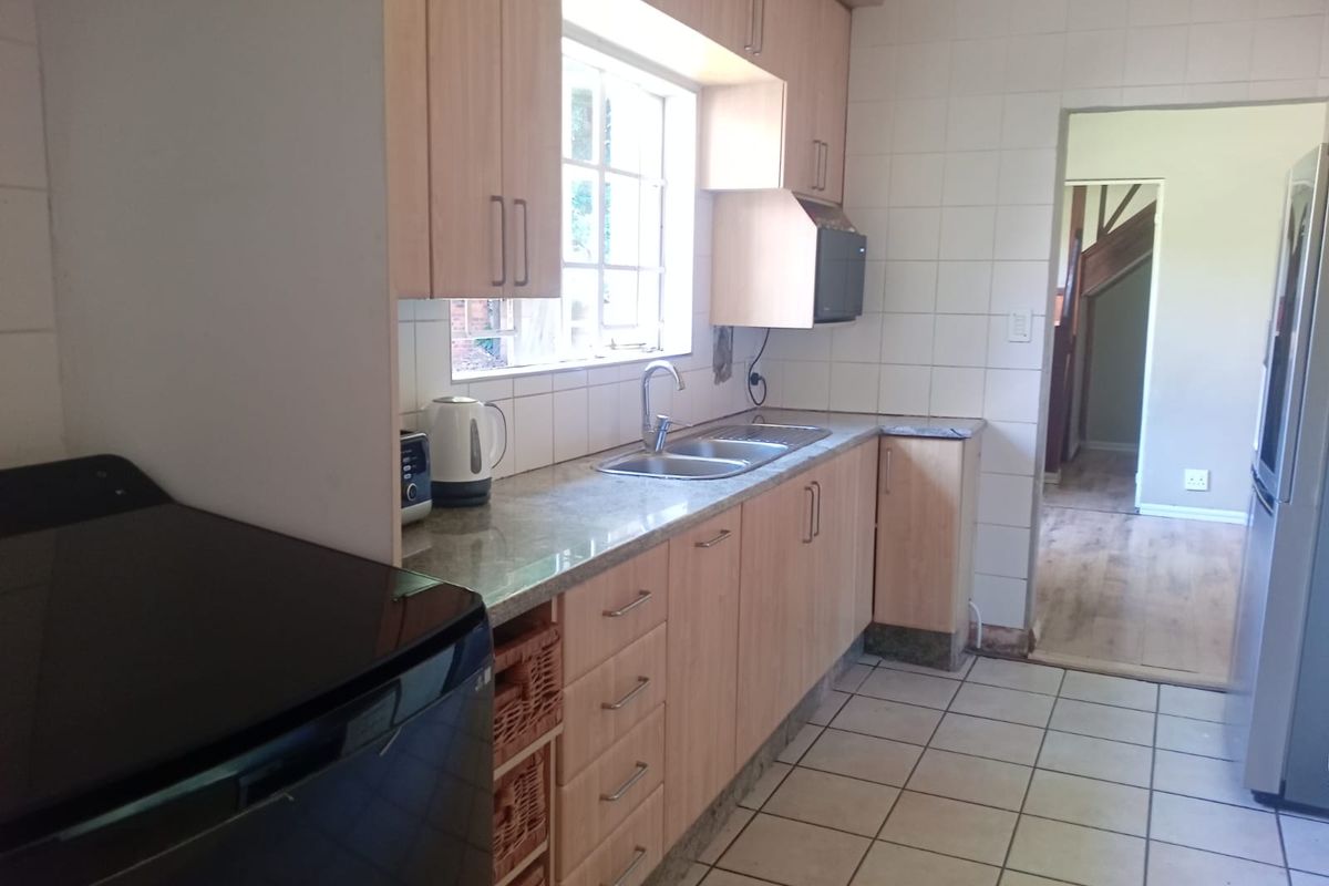 Functional kitchen featuring light wood cabinetry, stone countertops, double basin sink, and tiled finishes, offering a practical layout with direct access to the hallway.