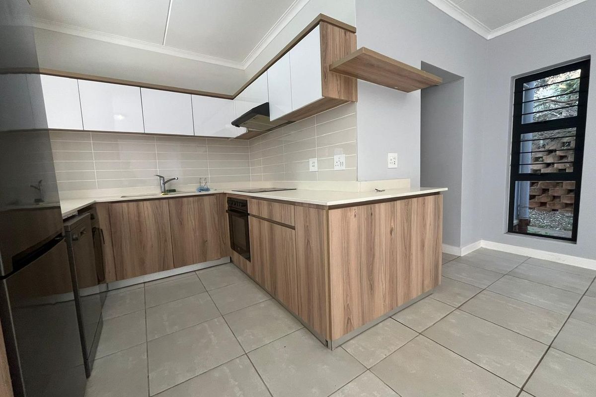 Modern kitchen featuring wood-grain and white cabinetry, stone countertops, integrated oven, cooktop, extractor fan, and neutral tiled flooring.