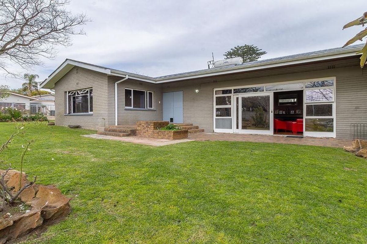 Rear view of the house featuring a brick patio, sliding glass doors, and a well-maintained garden with a brick planter box.