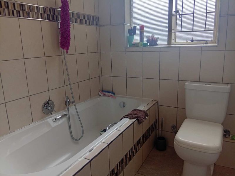 A functional bathroom featuring a bathtub with shower mixer, a standard toilet, and tiled wall finishes with decorative accents.