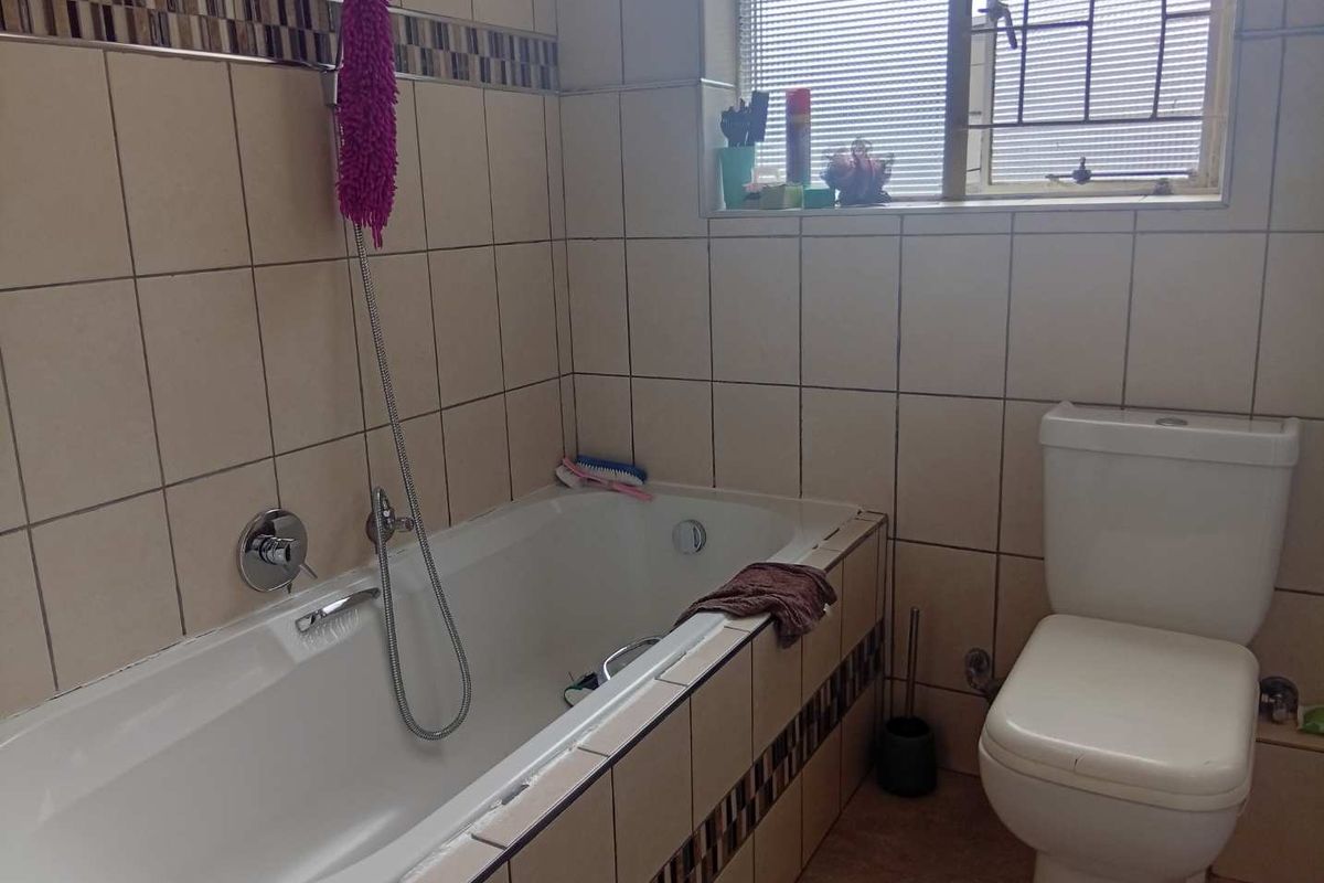 A functional bathroom featuring a bathtub with shower mixer, a standard toilet, and tiled wall finishes with decorative accents.