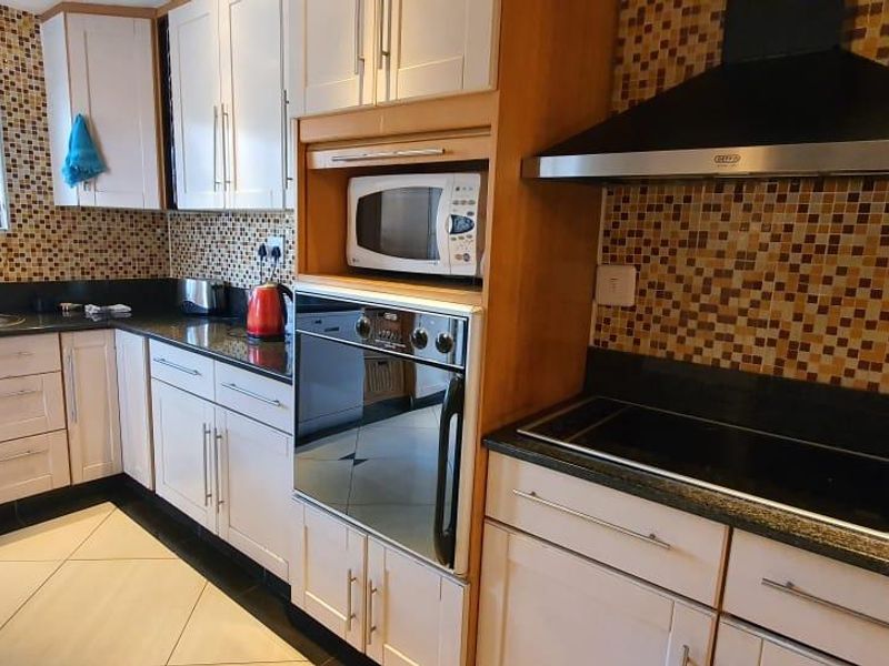 A functional kitchen featuring built-in cabinetry, granite countertops, a mosaic tile backsplash, and integrated appliances including an oven, microwave, and electric hob.