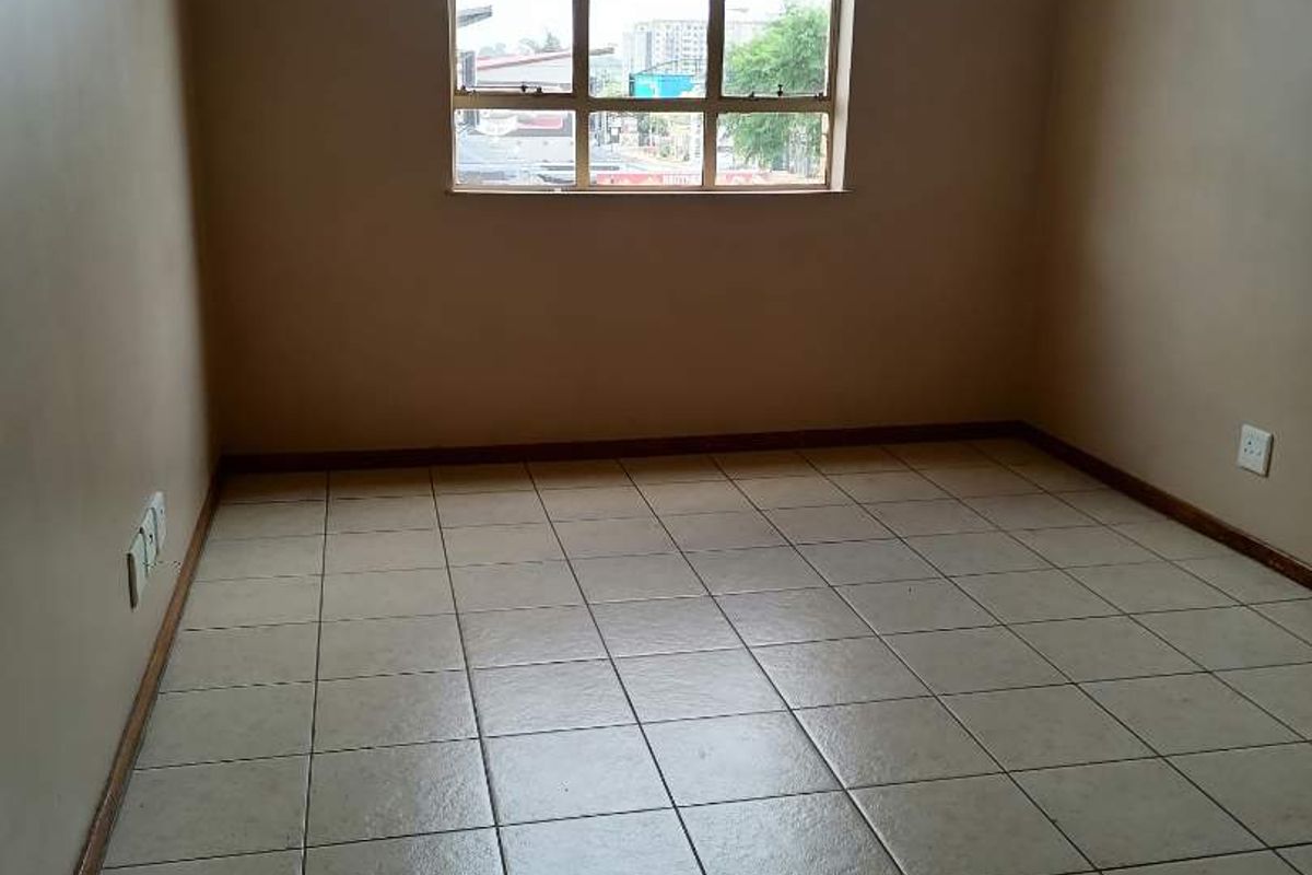 An empty bedroom featuring neutral tiled flooring and a large window providing natural light, ready for personalization.