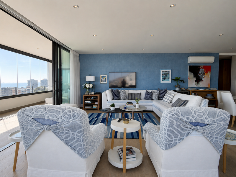 Spacious living room featuring textured blue accent wall, recessed lighting, and large sliding glass doors opening to a balcony with city views.