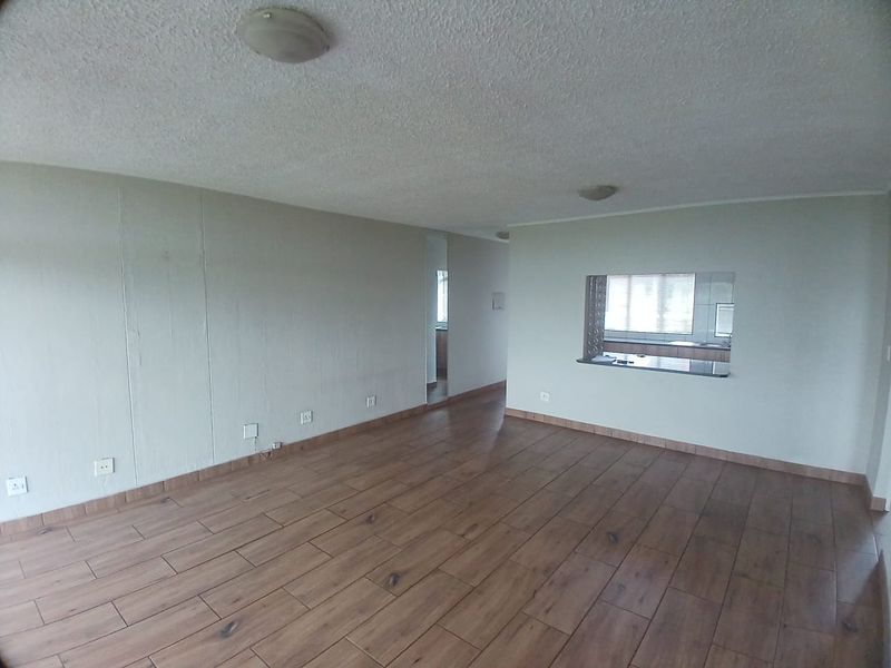 Spacious open-plan living area featuring wood-look tile flooring and a convenient kitchen serving hatch with a granite countertop.