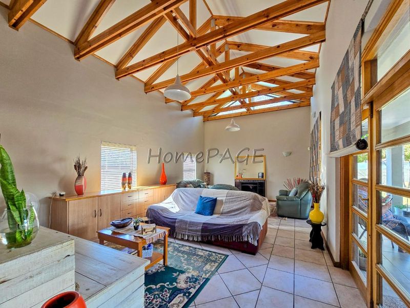 Spacious living room featuring high vaulted ceilings with exposed timber trusses, tiled flooring, built-in cabinetry, and a fireplace, opening to the outdoors.