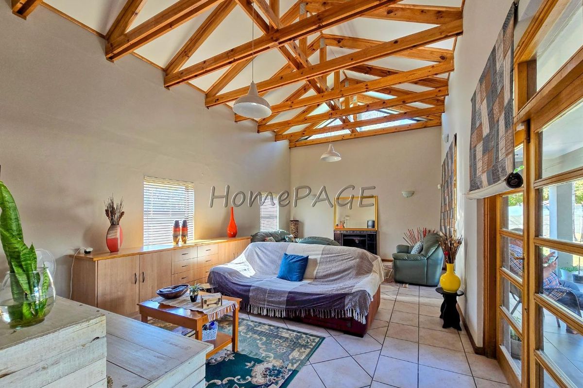 Spacious living room featuring high vaulted ceilings with exposed timber trusses, tiled flooring, built-in cabinetry, and a fireplace, opening to the outdoors.