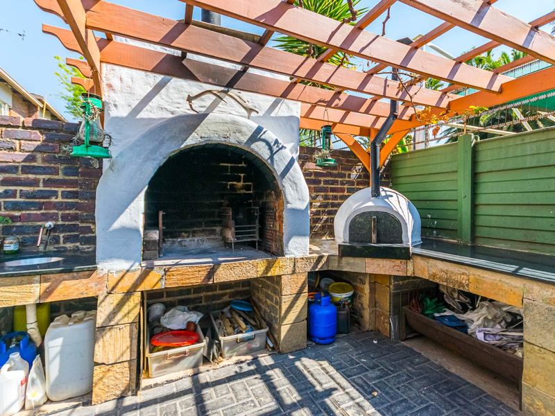 Outdoor entertainment area featuring a built-in braai, pizza oven, stone countertops, and a timber pergola structure.