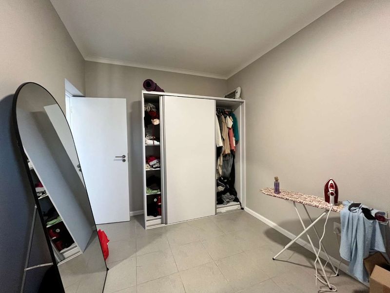 A bedroom featuring neutral wall tones, tiled flooring, and a built-in sliding door wardrobe providing ample storage space.