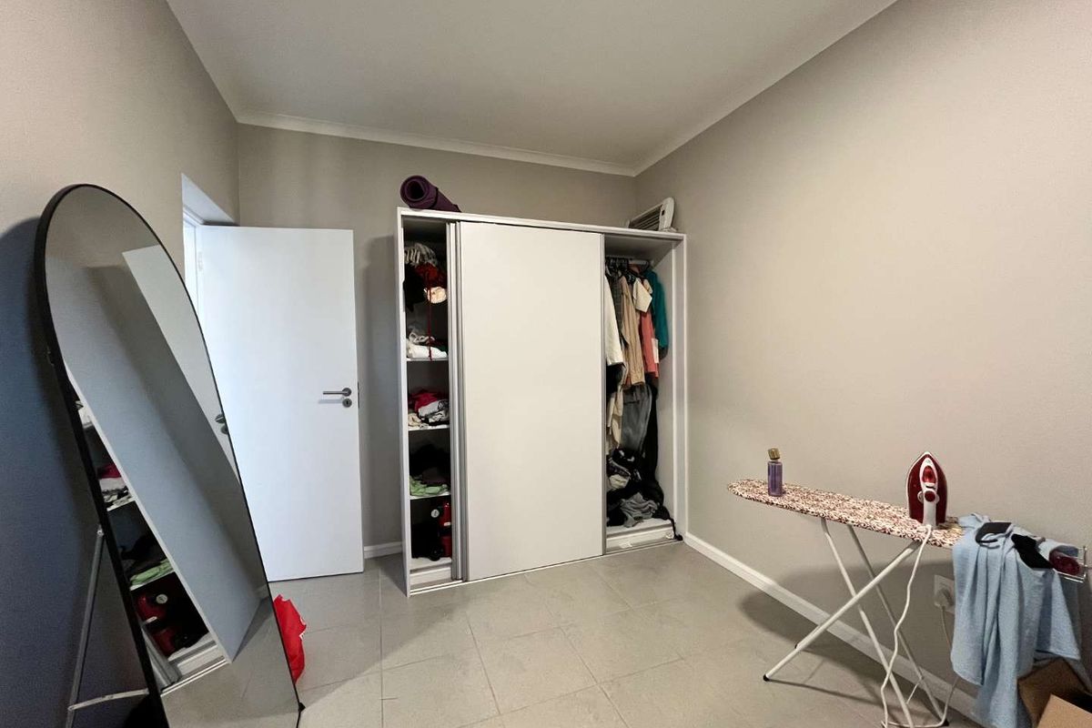 A bedroom featuring neutral wall tones, tiled flooring, and a built-in sliding door wardrobe providing ample storage space.
