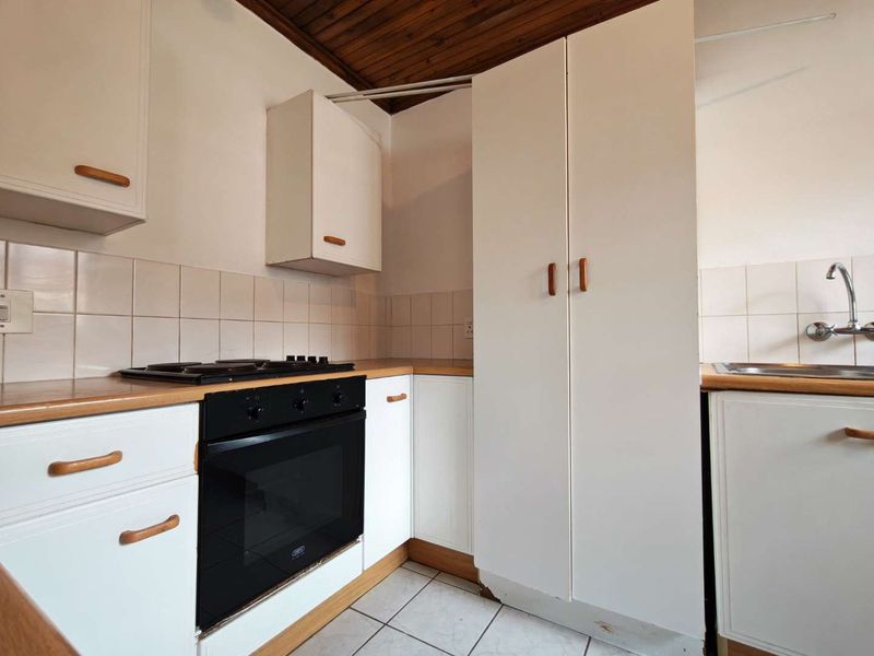 A dated kitchen featuring white cabinetry, a built-in oven with gas hob, tiled backsplash, and a timber ceiling.