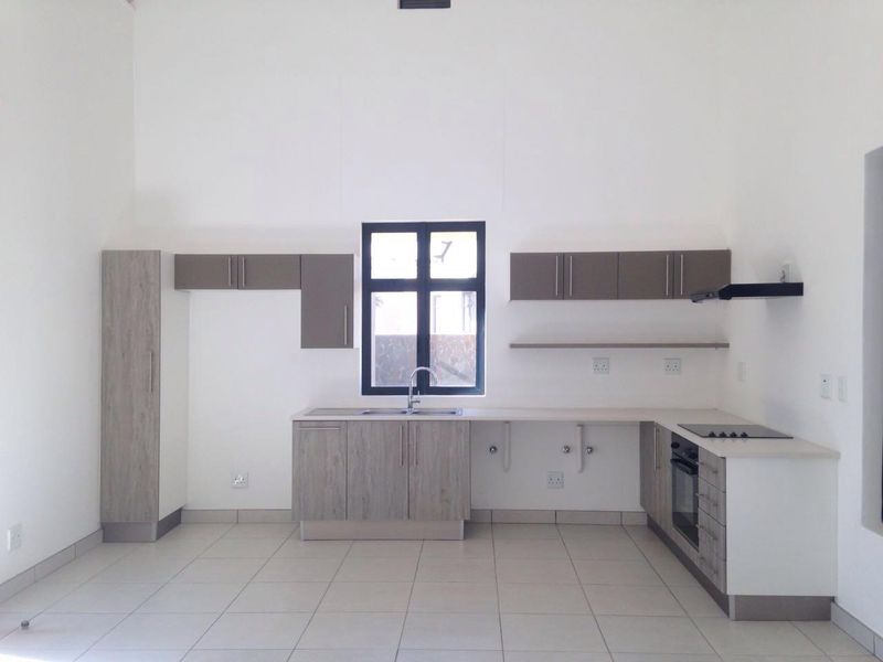 A modern, empty kitchen featuring light wood-grain cabinetry, integrated oven and hob, tiled flooring, and a central window providing natural light.