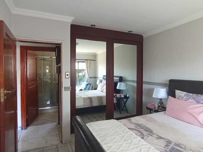 Spacious bedroom featuring a large built-in mirrored wardrobe, crown molding, and direct access to an en-suite bathroom.