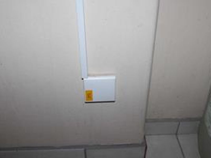 A close-up view of a utility area featuring surface-mounted electrical conduit and a junction box on a plain wall with tiled flooring.