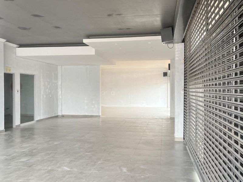 Spacious open-plan retail area featuring tiled flooring, a modern recessed ceiling design, and a secure metal roller shutter entrance.