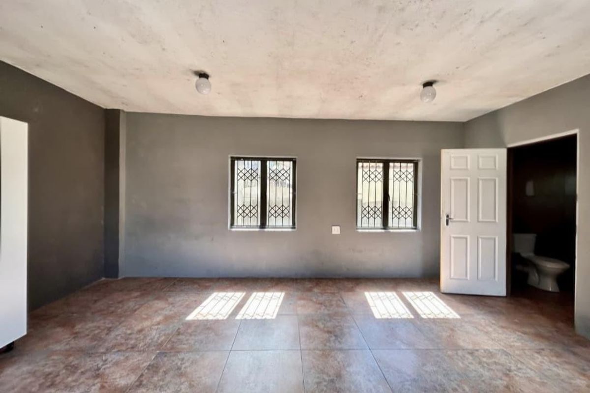 An empty bedroom featuring tiled flooring, security bars on windows, and a neutral grey wall finish, requiring minor cosmetic updates to the ceiling.
