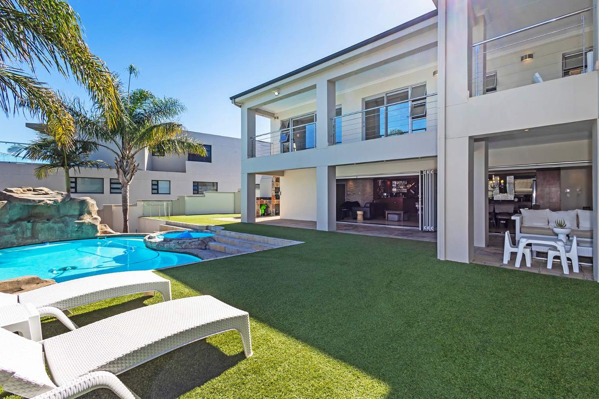 Rear exterior view featuring a swimming pool, artificial lawn, covered patio, and upper-level balcony with modern stainless steel balustrades.