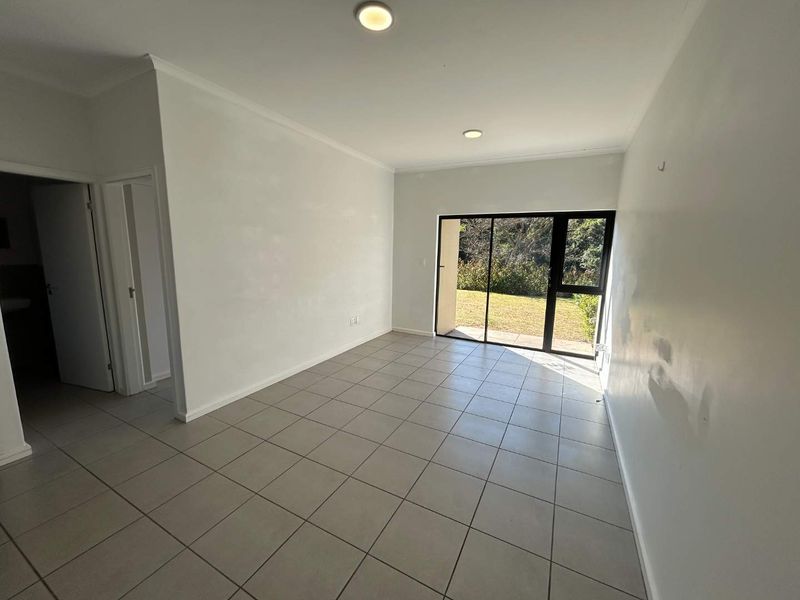 An empty, open-plan living area featuring neutral floor tiles, recessed lighting, and a large sliding glass door providing access to the garden.