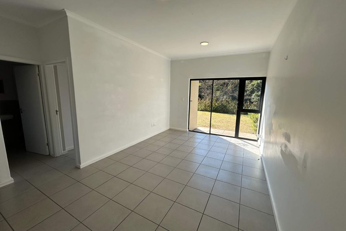 An empty, open-plan living area featuring neutral floor tiles, recessed lighting, and a large sliding glass door providing access to the garden.