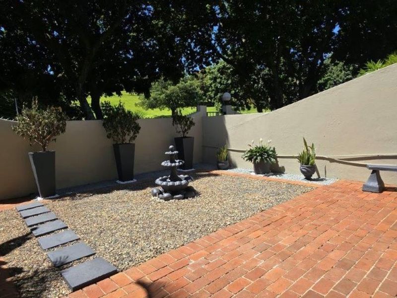 A well-maintained rear courtyard featuring brick paving, gravel landscaping, a decorative stone fountain, and a solid boundary wall.
