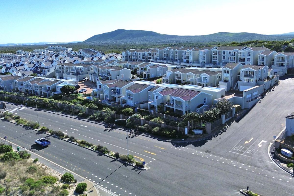 Aerial view of a residential townhouse complex featuring multiple units with tiled roofs, balconies, and paved driveways, situated near a main road.