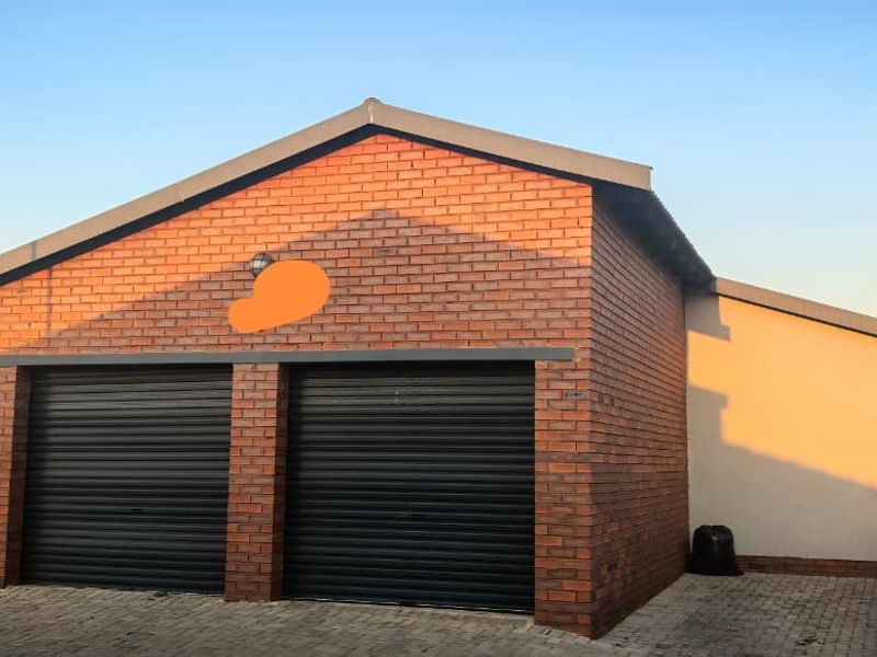A well-maintained double garage featuring face brick construction and black roller doors, situated on a paved driveway.