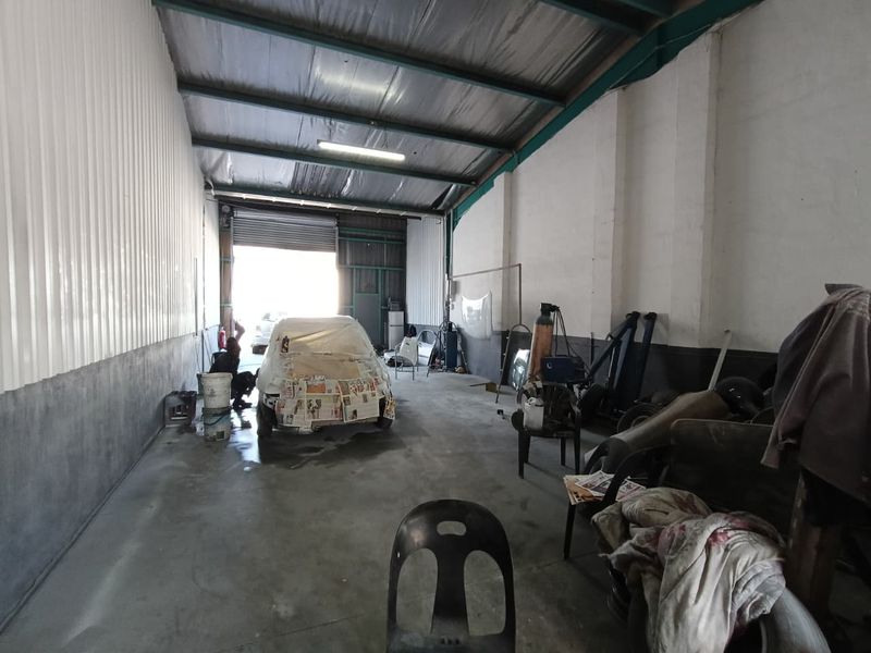 Industrial utility space featuring high ceilings with exposed steel trusses, concrete flooring, and a large roller shutter door for vehicle or equipment access.