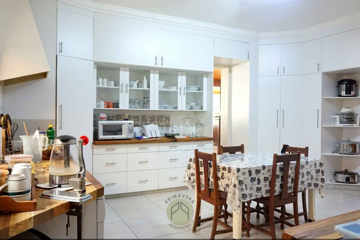 A spacious kitchen featuring white built-in cabinetry, wooden countertops, an extractor fan, and tiled flooring, offering ample storage and a functional layout.