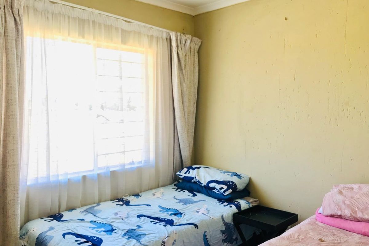 A bedroom featuring a sliding window with curtains and textured wall surfaces requiring maintenance and cosmetic updates.