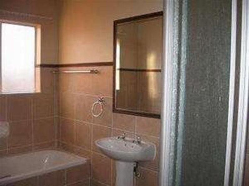 A functional bathroom featuring a pedestal basin, bathtub, and separate shower enclosure with neutral wall tiling.