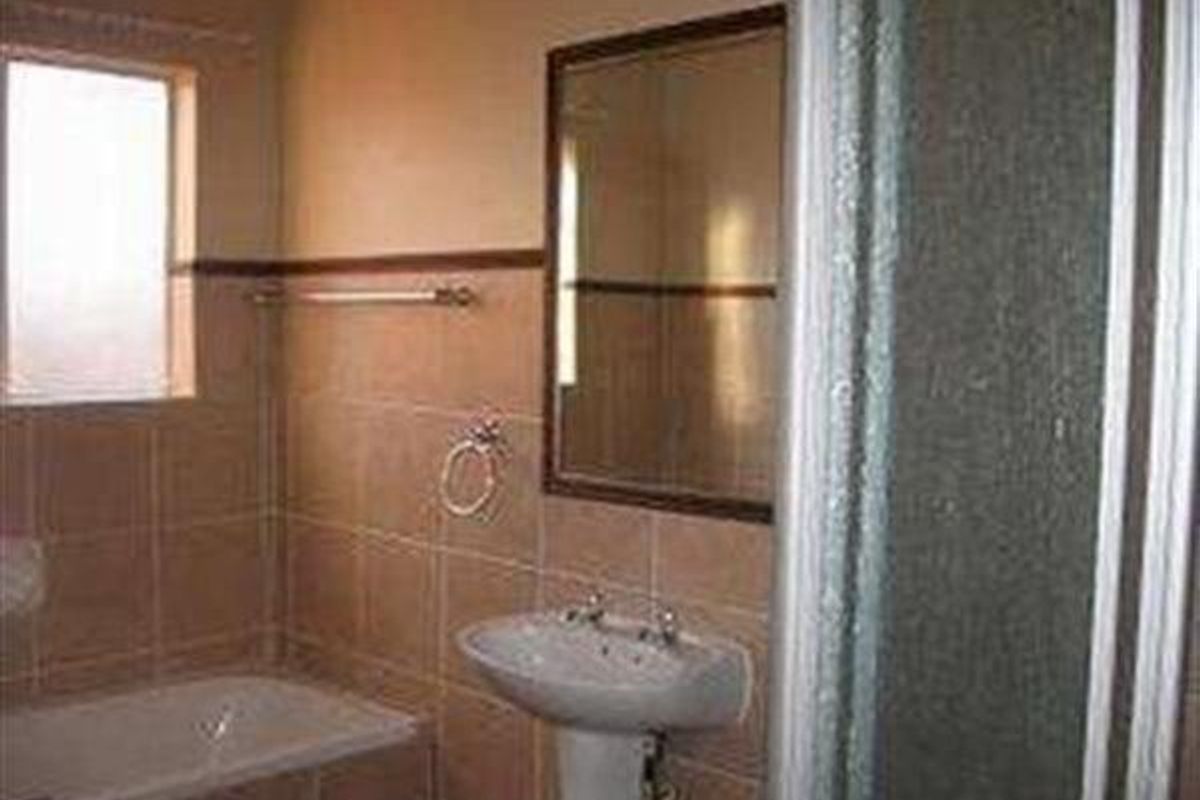A functional bathroom featuring a pedestal basin, bathtub, and separate shower enclosure with neutral wall tiling.
