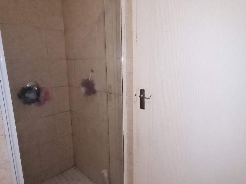 A functional bathroom featuring a tiled shower enclosure with a glass door and neutral wall tiling.