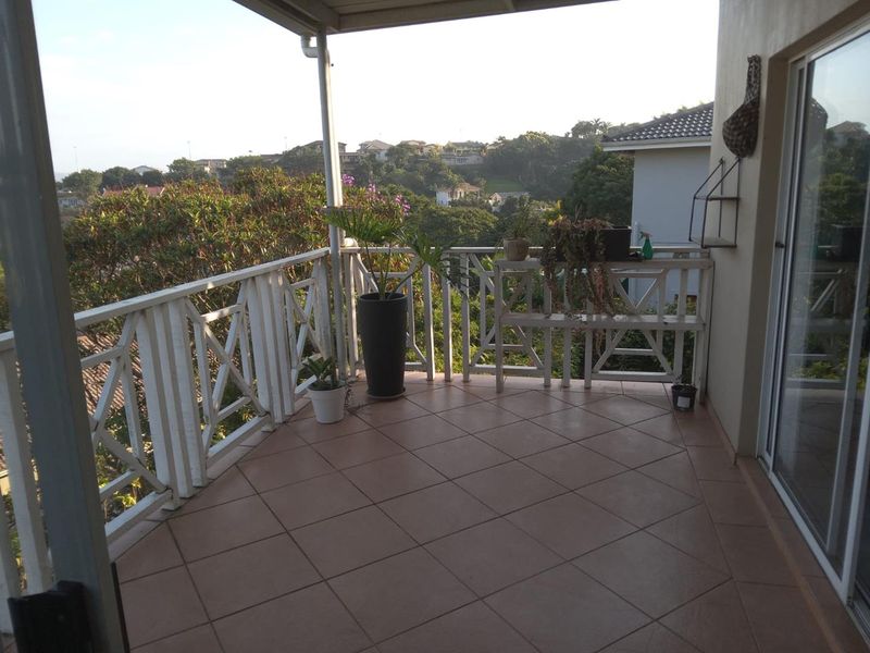 A covered balcony featuring tiled flooring and a wooden balustrade, offering elevated views of the surrounding neighborhood.