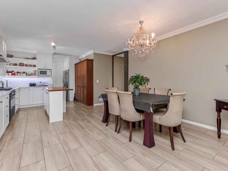 Spacious open-plan kitchen and dining area featuring modern white cabinetry, a central island, tiled flooring, and an elegant chandelier.