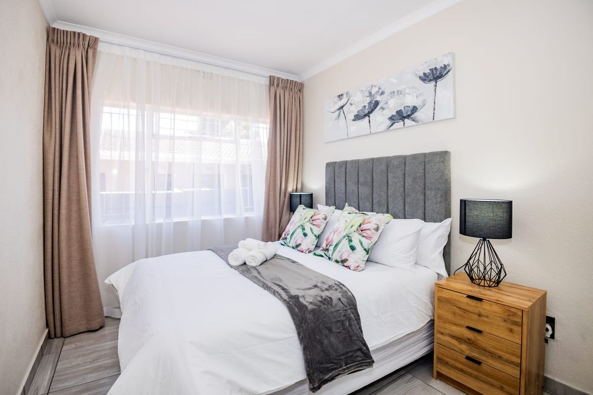 A well-maintained bedroom featuring neutral wall finishes, modern wood-look flooring, and large windows with fitted curtain tracks.
