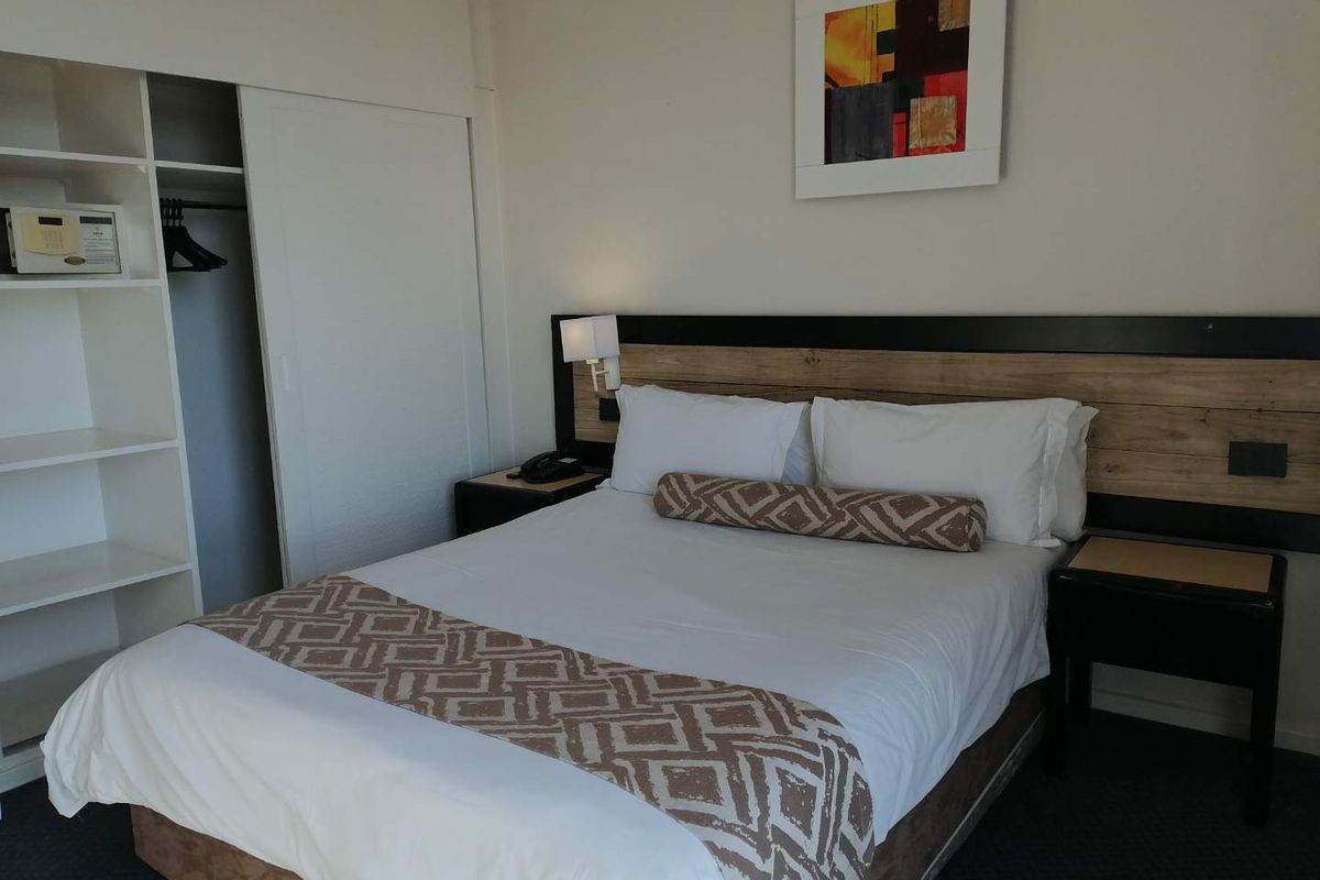 A bedroom featuring a built-in wardrobe with shelving and a wall-mounted headboard with integrated lighting.