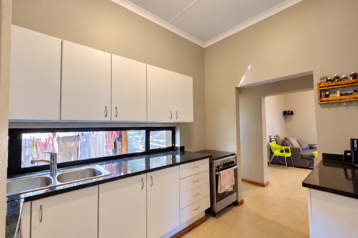 Functional kitchen featuring white cabinetry, black granite countertops, and a stainless steel double sink, with an adjacent living area visible through the doorway.