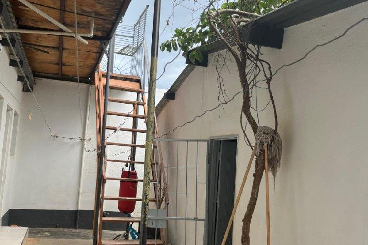 Exterior rear courtyard area featuring a metal staircase, covered patio section with plywood ceiling, and paved flooring.