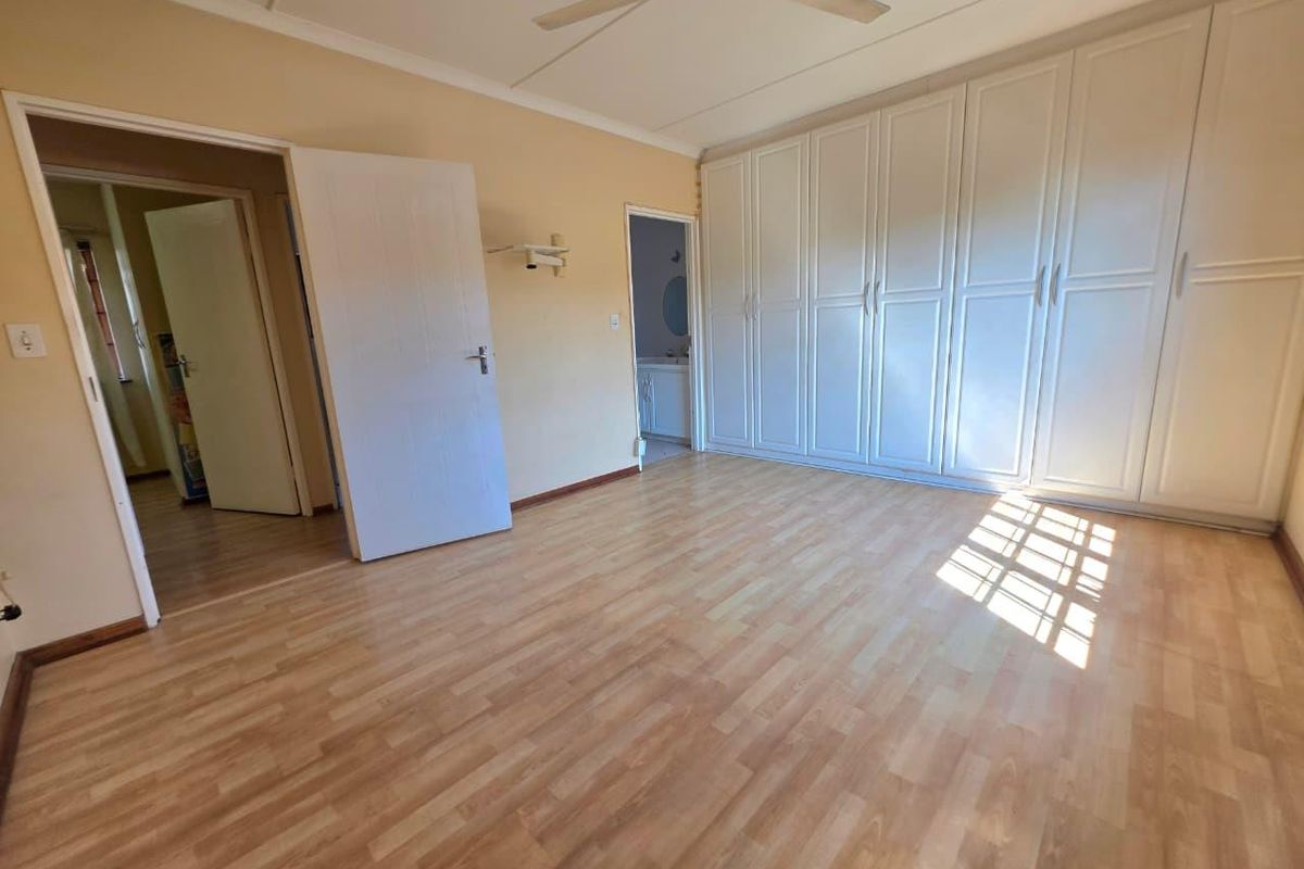 A spacious bedroom featuring light wood-look laminate flooring, a large wall-to-wall built-in wardrobe, and a ceiling fan.