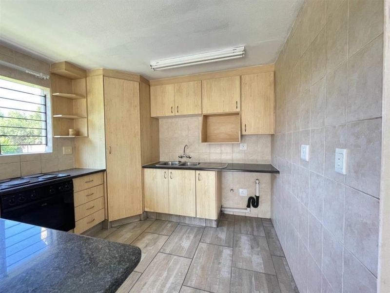 A functional kitchen featuring light wood-tone cabinetry, tiled flooring, a double sink, and a built-in stove, offering a clean and practical workspace.