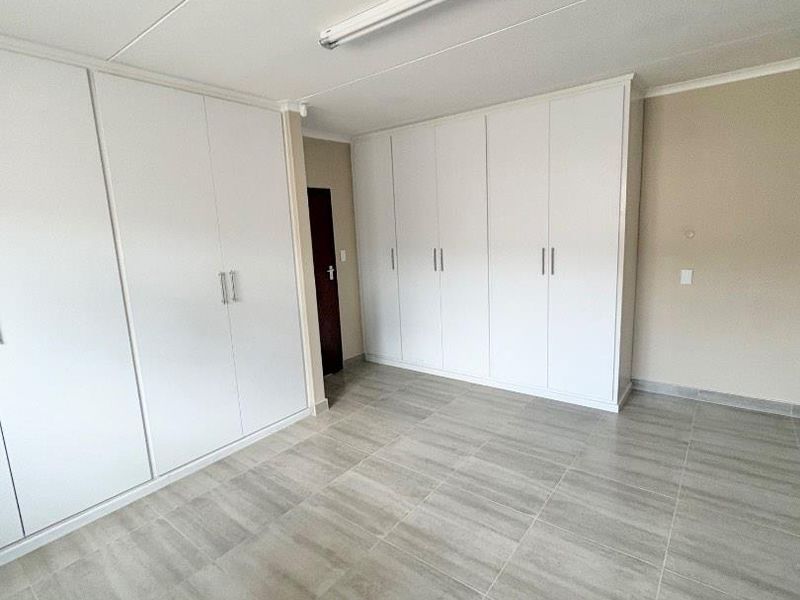 A clean, empty office space featuring neutral tiled flooring and extensive built-in white cabinetry for storage.