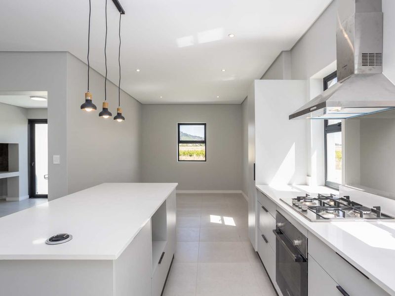 Modern, minimalist kitchen featuring a central island, stone countertops, built-in gas hob, oven, and extractor fan with clean, neutral finishes.