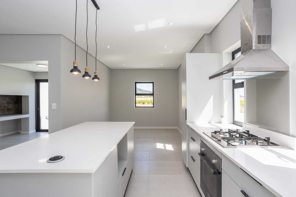 Modern, minimalist kitchen featuring a central island, stone countertops, built-in gas hob, oven, and extractor fan with clean, neutral finishes.