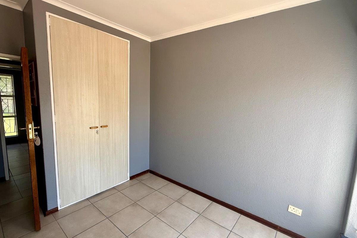 An empty bedroom featuring grey painted walls, tiled flooring, and a built-in wardrobe with light wood-finish doors.