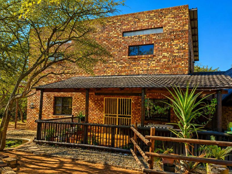 A two-story exposed brick house featuring a covered patio with timber railings and secure entrance, set within a natural garden environment.