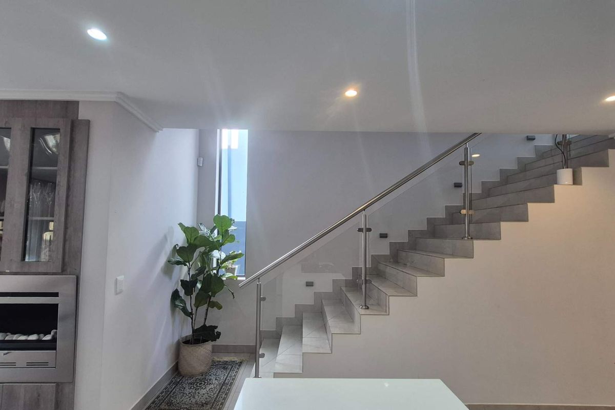 Modern living area featuring a sleek built-in fireplace, tiled staircase with a contemporary glass and stainless steel balustrade, and recessed lighting.