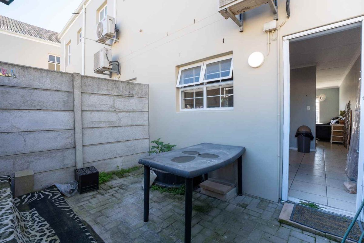 A paved rear courtyard area featuring a precast concrete boundary wall and external air conditioning units, providing access to the interior living space.