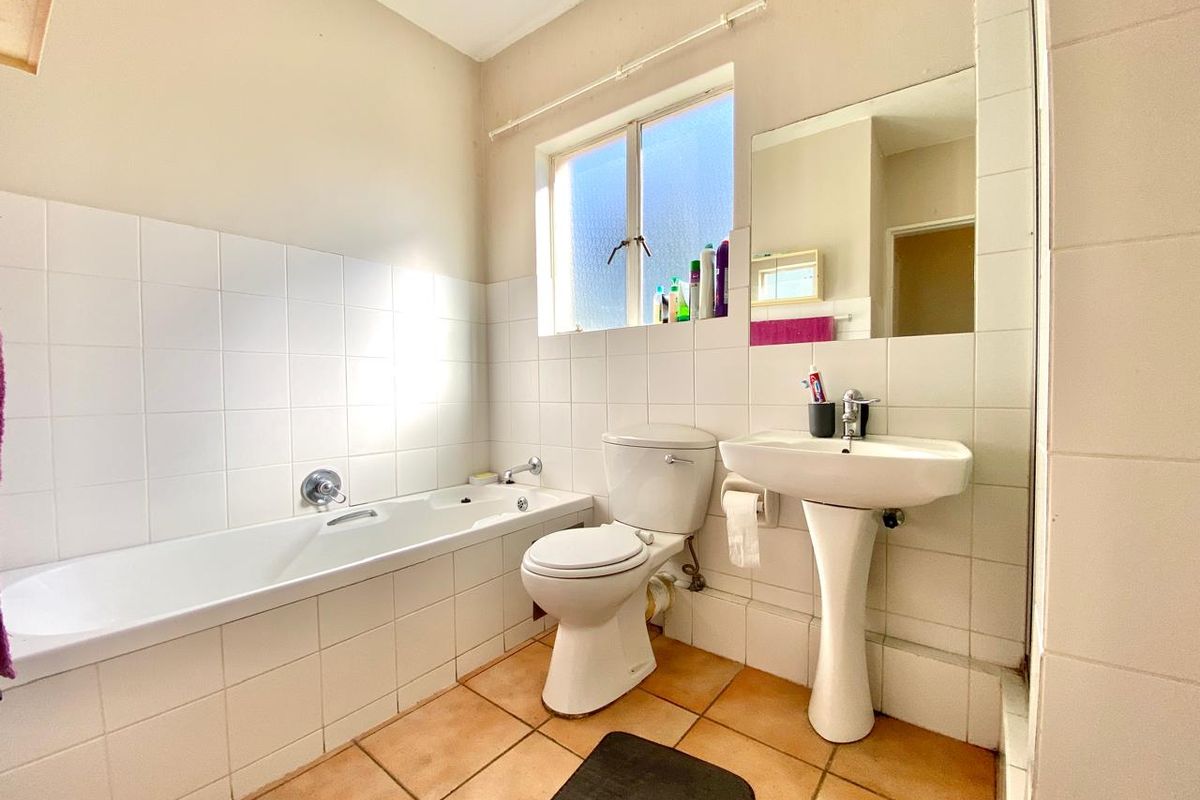 A functional bathroom featuring a white bathtub, pedestal basin, and toilet with tiled walls and flooring.