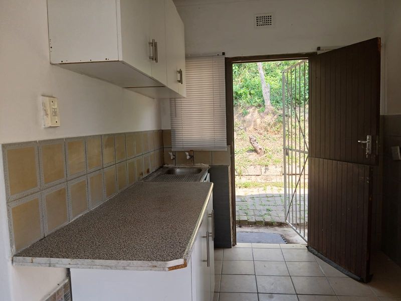 A compact kitchen area featuring built-in cabinetry, a laminate countertop, and a stainless steel sink, with direct access to an outdoor area.